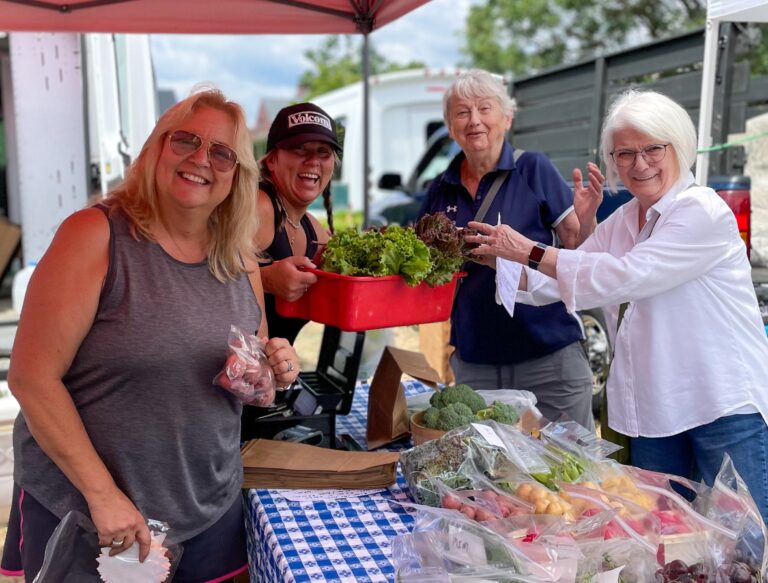 four smiling women holding vegetables