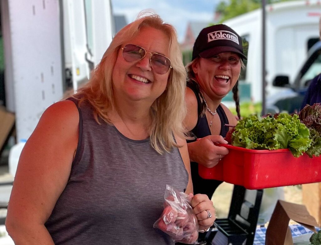 four smiling women holding vegetables