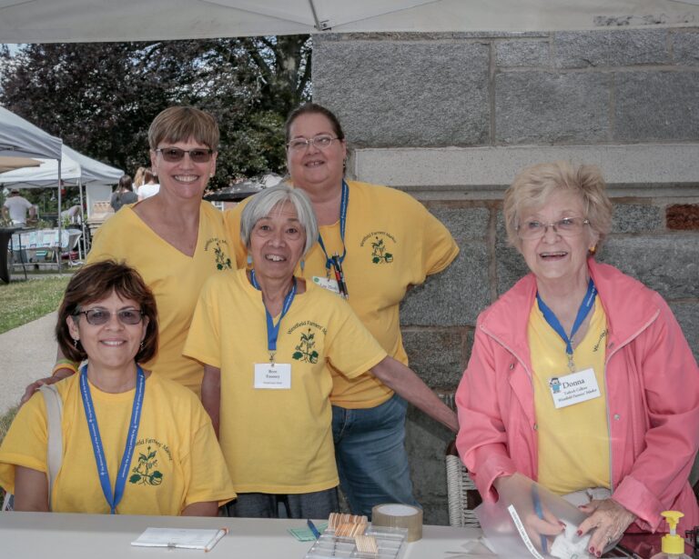 Five smiling women wearing yellow shirts.