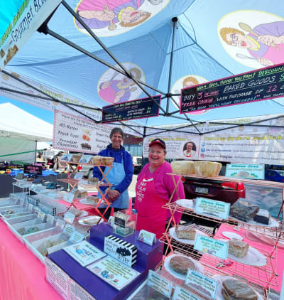 Smiling woman in bright pink apron surrounds by baked goods on display